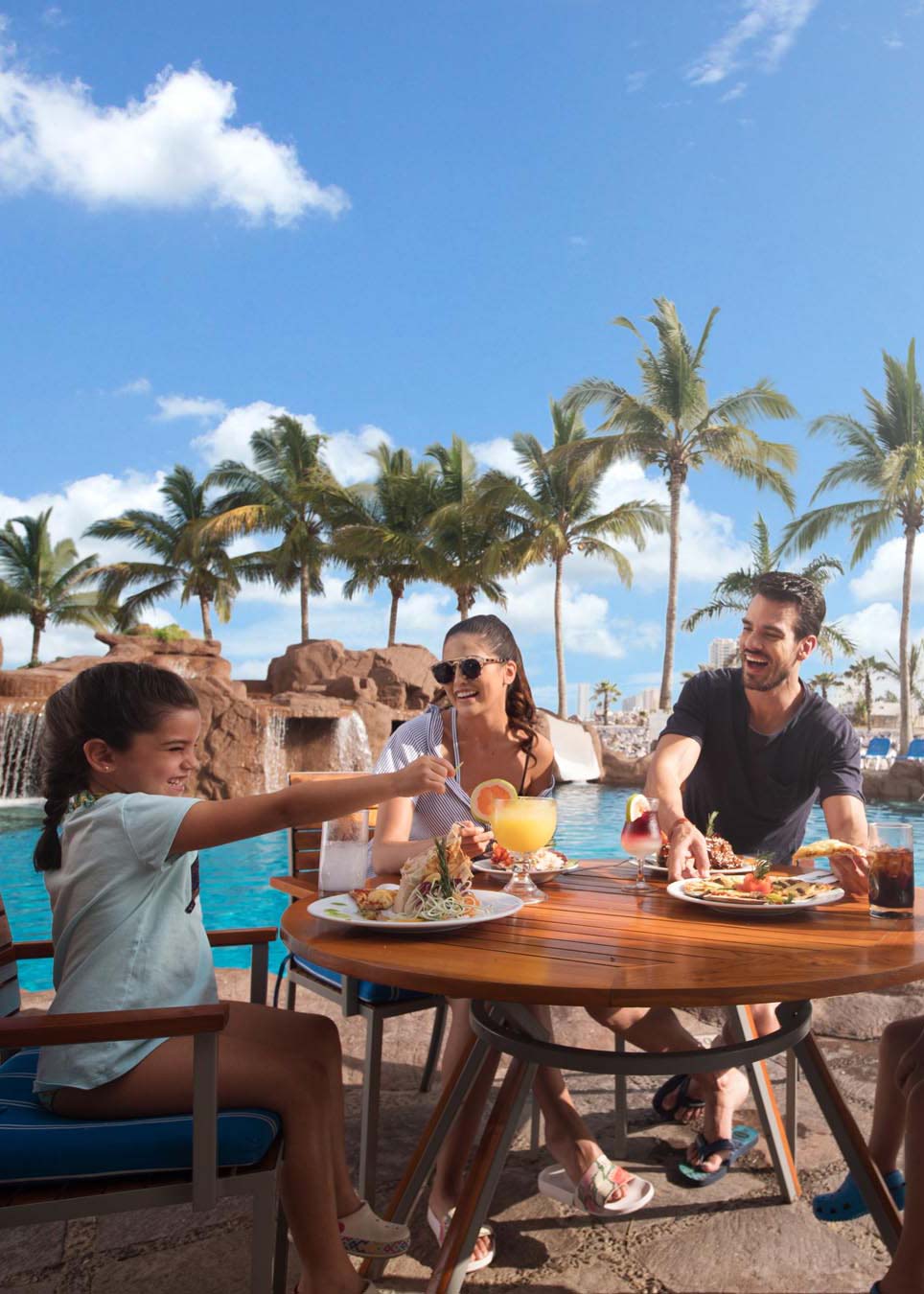 Man and woman sitting at swim up bar with pool and palm trees in background