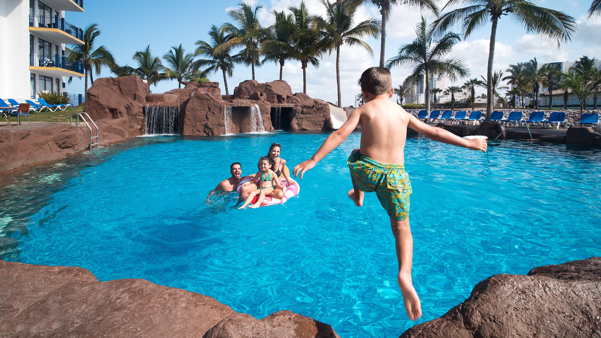 Child jumping into the pool as parents relax in the water nearby