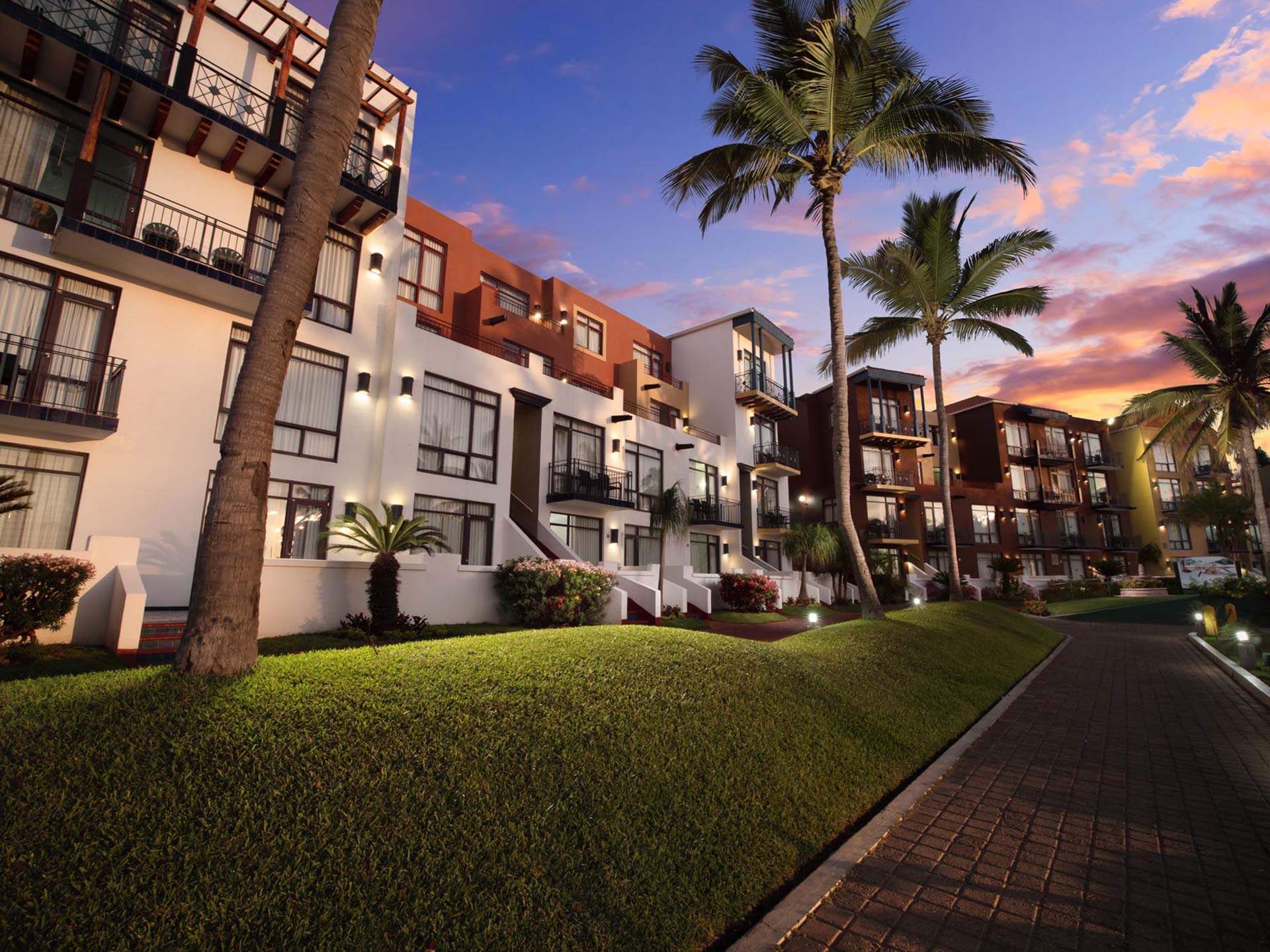 White resort buildings beside palm trees and sky with sunset