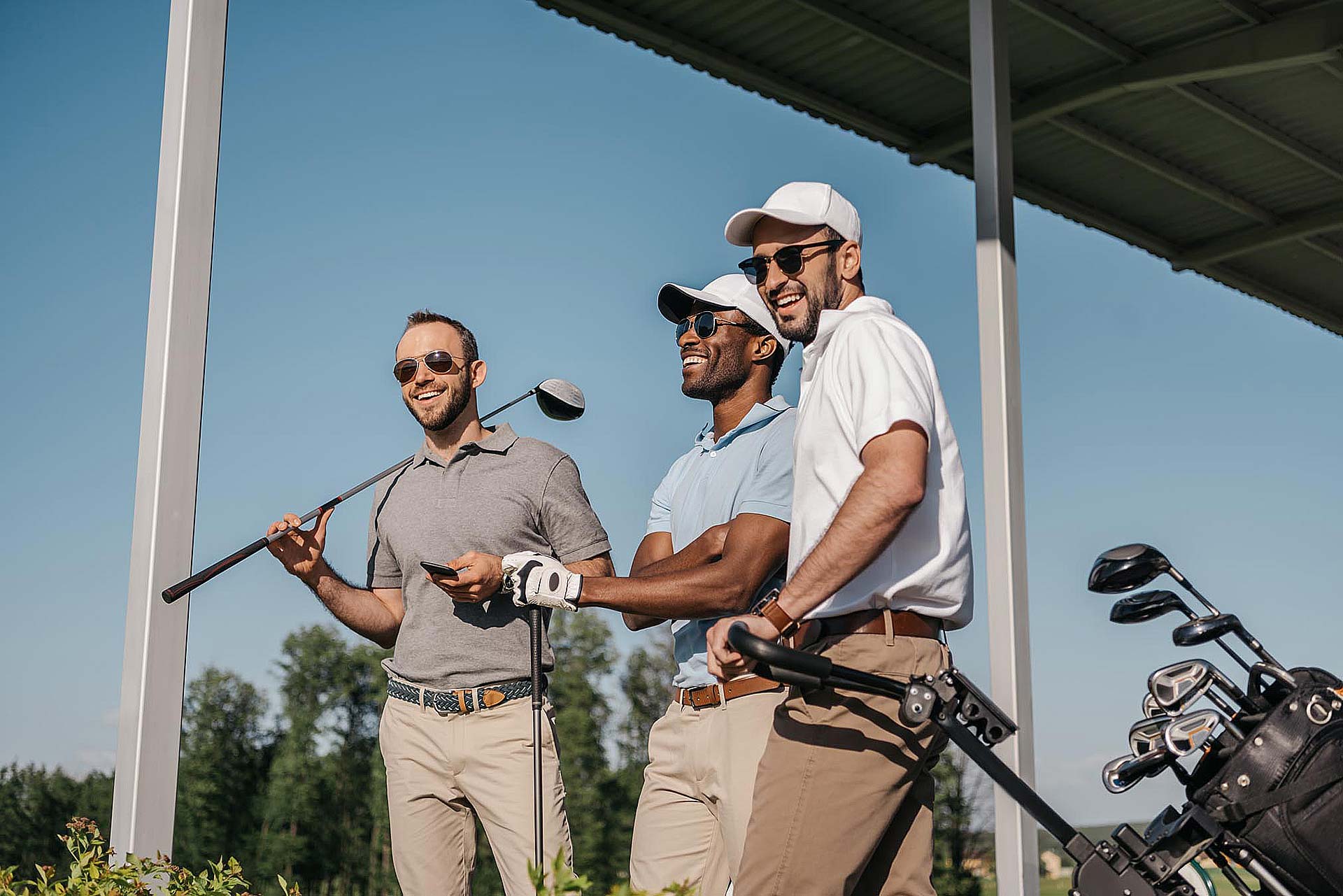 Three golfers smile while holding golf clubs