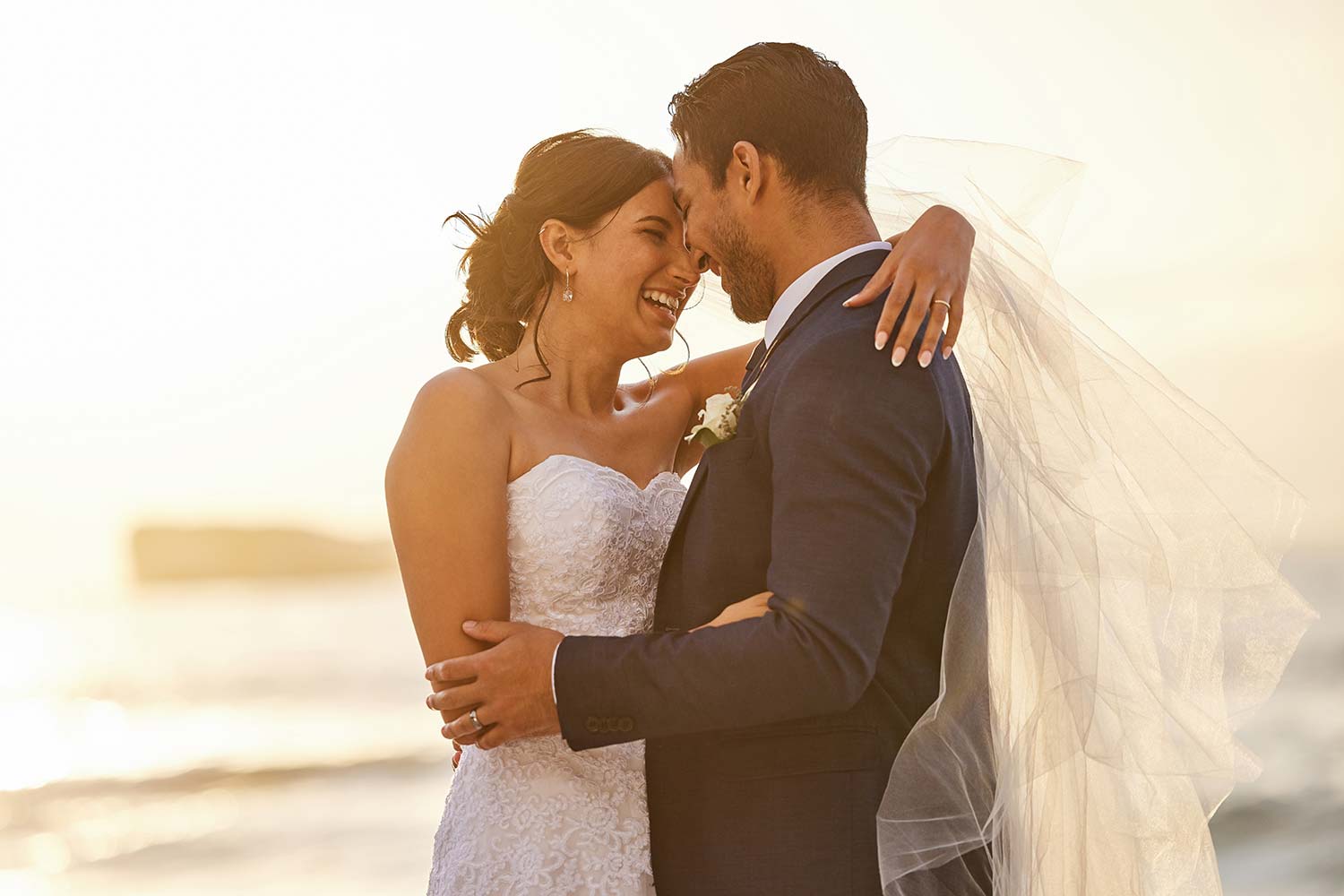 Bride and grooming hugging in front of a beach